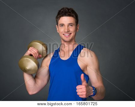 Handsome power athletic man in training pumping up muscles with dumbbells in a gym. blue t-shirt
