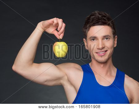 Portrait of young smiling bodybuilder holding apple in black background.