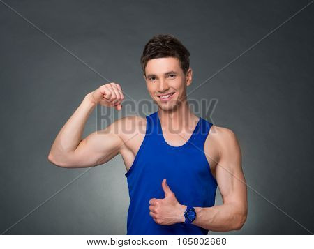 Handsome man showing off bicep and thumb up on black background, blue t-shirt