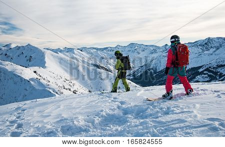 Two snowboarders on the mountain top just before riding down the