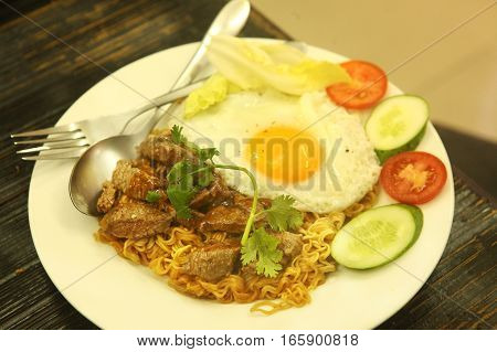 fried eggs served in frying pan with moodles beef cucumber and cut tomato