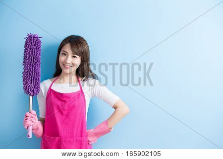beauty housewife take feather duster and smile to you isolated on blue background asian