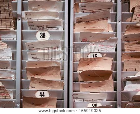 A rack of time cards used by factory workers in conjunction with a time clock to prove the hours they worked. Please note visible German language on the cards.