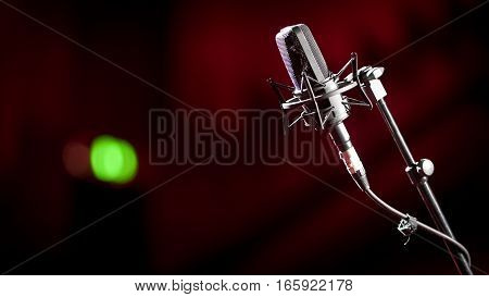 Shallow focus on a stand mounted condenser microphone with a green recording light showing in the background blur.
