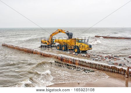 excavator loading a truck stones on the beachon cold winter day