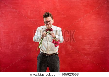 The young funny man with broken bouquet on red studio background. Concept - unhappy love