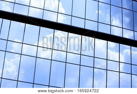 Abstract full frame office windows of an anonymous city skyscraper reflecting the blue sky and clouds.