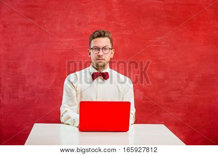 Young disappointed funny man with laptop at St. Valentine's Day on red studio background with copy space