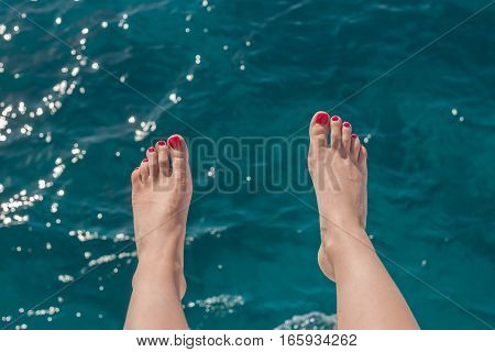 wooman feet with red nails on blue sea background