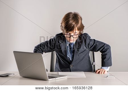 Schoolchild in business suit standing over desk and looking angry at camera
