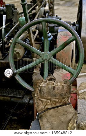 A gloved hand operates the steering wheel of a very old steam driven tractor