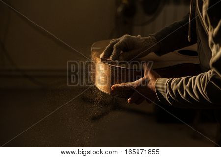 Serious professional guitar-maker working with unfinished guitar at workshop.