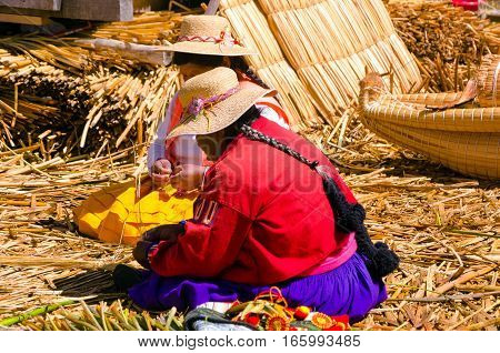UROS FLOATING ISLANDS PERU - SEPTEMBER 19: Women make handicrafts on one of the Uros Floating Islands in Peru on Lake Titicaca on September 19 2014