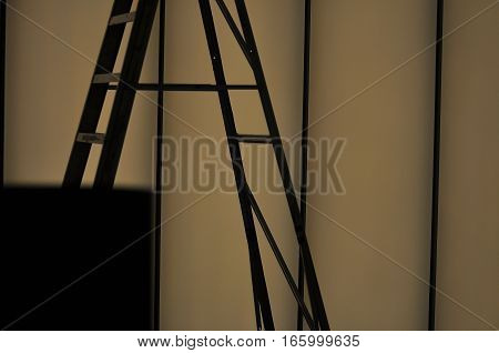 Close up silhouette of a ladder and a dimly lit wall