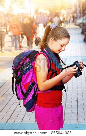 Tourist girl kid with backpack taking pictures on digital camera at sight cultural city pedestrianized street outdoor. Child view photos on digital camera