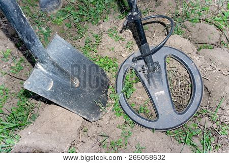 Metal Detector Coil Over A Metal Object Protruding From The Ground. A Shovel Driven Into The Ground 