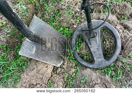 Metal Detector Coil Over A Metal Object Protruding From The Ground. A Shovel Driven Into The Ground 