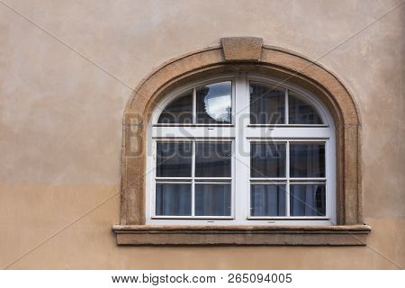 Wall Of A House In Tones Of Brown Color With A Window With Stone Frame With An Arch. White Curtains 