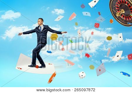 A Businessman Flies Standing On A Large Playing Card And Surrounded By Flying Cards, Chips And Dice.