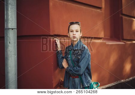 Curious Little Girl In Jeans Clothes Stands Near An Old Restored Beautiful Building.