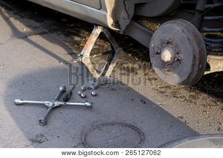 Replacing The Rear Wheel Of The Car. The Car Is Mounted On The Jack. On Asphalt Lie Screws, Tool And