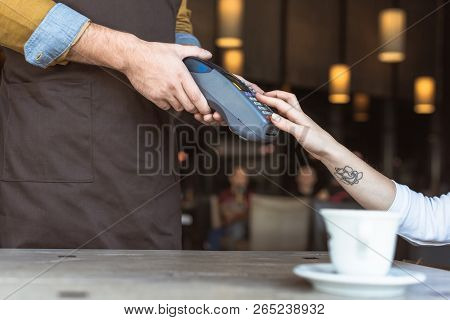 Cropped Shot Of Waiter Holding Payment Terminal While Client Entering Pin In Cafe