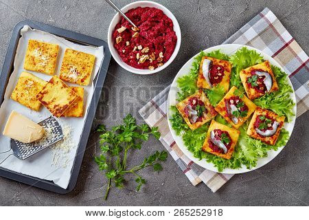 Polenta Squares With Creamy Beetroot Puree, Topped With Anchovies And Parsley On A White Plate. Fres