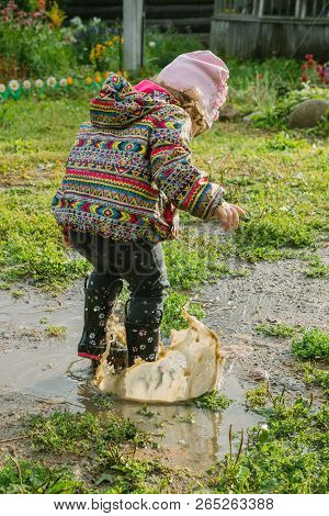 Little Girl In Boots Trampling A Muddy Puddle In Autumn