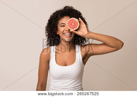 Happy Young Black Woman Holding Half Of Grapefruit On Light Background
