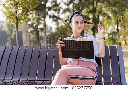Beautiful  Young Woman  Holding  Open Book And Reading On Bench In Autumn Park