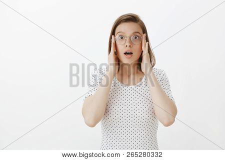 Portrait Of Shocked Caucasian Girl In Glasses And T-shirt, Holding Hands On Face, Dropping Jaw And G