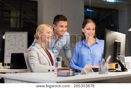 business, deadline and technology concept - coworkers with computer working late at night office