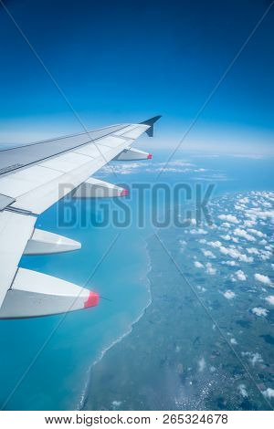 View From Airplane Window With Wing Flying Over Coastline And Ocean With Clouds, West Coast, North I