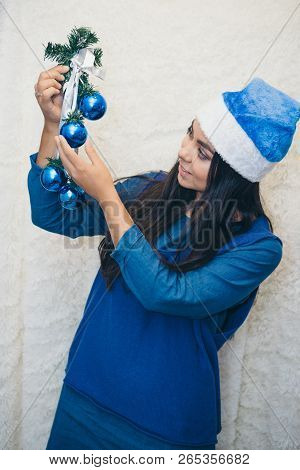 The Girl In A Blue Dress And A Blue Christmas Hat Holding Blue Balloons. Beautiful Brunette Smiled E