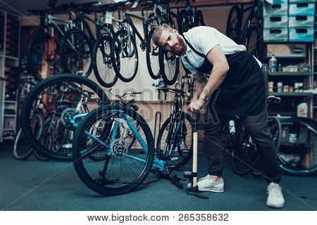 Guy Pumps Bicycle Wheel With Air In Bike Workshop. Portrait Of Young Bearded Bicycle Mechanic Wearin