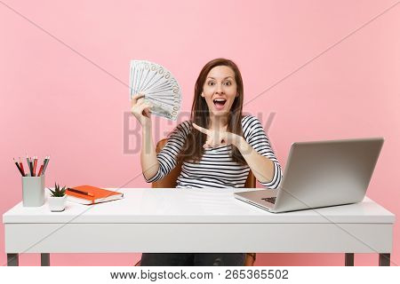 Young Amazed Woman Pointing Index Finger On Bundle Lots Of Dollars, Cash Money Work At Office At Whi