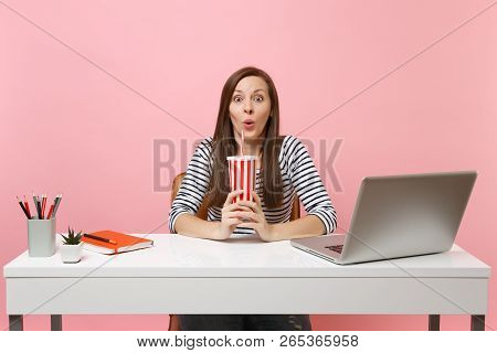 Young Amazed Funny Woman Holding Plactic Cup With Cola Or Soda Sit Work At White Desk With Contempor