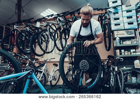 Young Mechanic Repairs Bicycle In Bike Workshop. Portrait Of Bearded Man Wearing White T-shirt And A