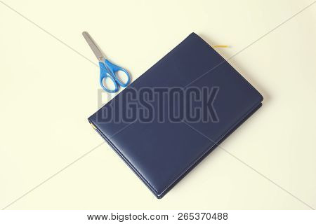Notepad And Blue Scissors On Yellow Background