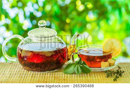 Tea time. Pouring out hot tea into a cup. Green nature background.