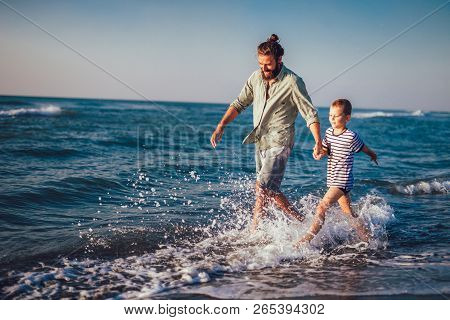 Happy Father And Son, Man & Boy Child, Running And Having Fun In The Sand And Waves Of A Sunny Beach