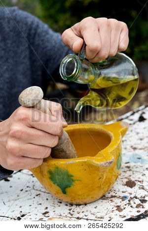 closeup of a young caucasian man outdoors making some aioli using a wooden pestle in a yellow ceramic mortar, by adding olive oil from a glass cruet