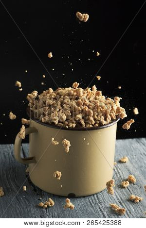 some chunks of textured soy protein in an old beige enamelware pot, placed on a rustic gray wooden table, against a black background