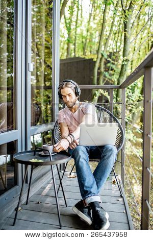 Poortrait Of A Handsome Man Working With Laptop On The Balcony Of The House In The Beautiful Green F