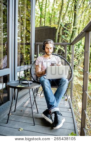 Poortrait Of A Handsome Man Working With Laptop On The Balcony Of The House In The Beautiful Green F
