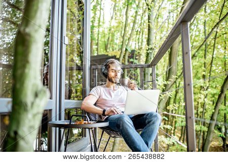 Poortrait Of A Handsome Man Working With Laptop On The Balcony Of The House In The Beautiful Green F