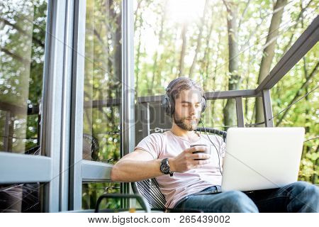 Poortrait Of A Handsome Man Working With Laptop On The Balcony Of The House In The Beautiful Green F