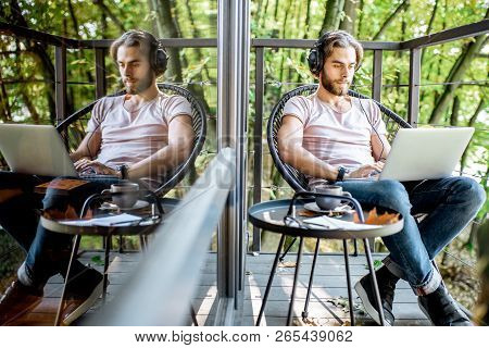 Poortrait Of A Handsome Man Working With Laptop On The Balcony Of The House In The Beautiful Green F