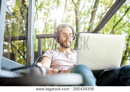 Poortrait Of A Handsome Man Working With Laptop On The Balcony Of The House In The Beautiful Green F