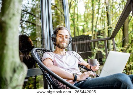 Poortrait Of A Handsome Man Working With Laptop And Headphones On The Balcony Of The House In The Be